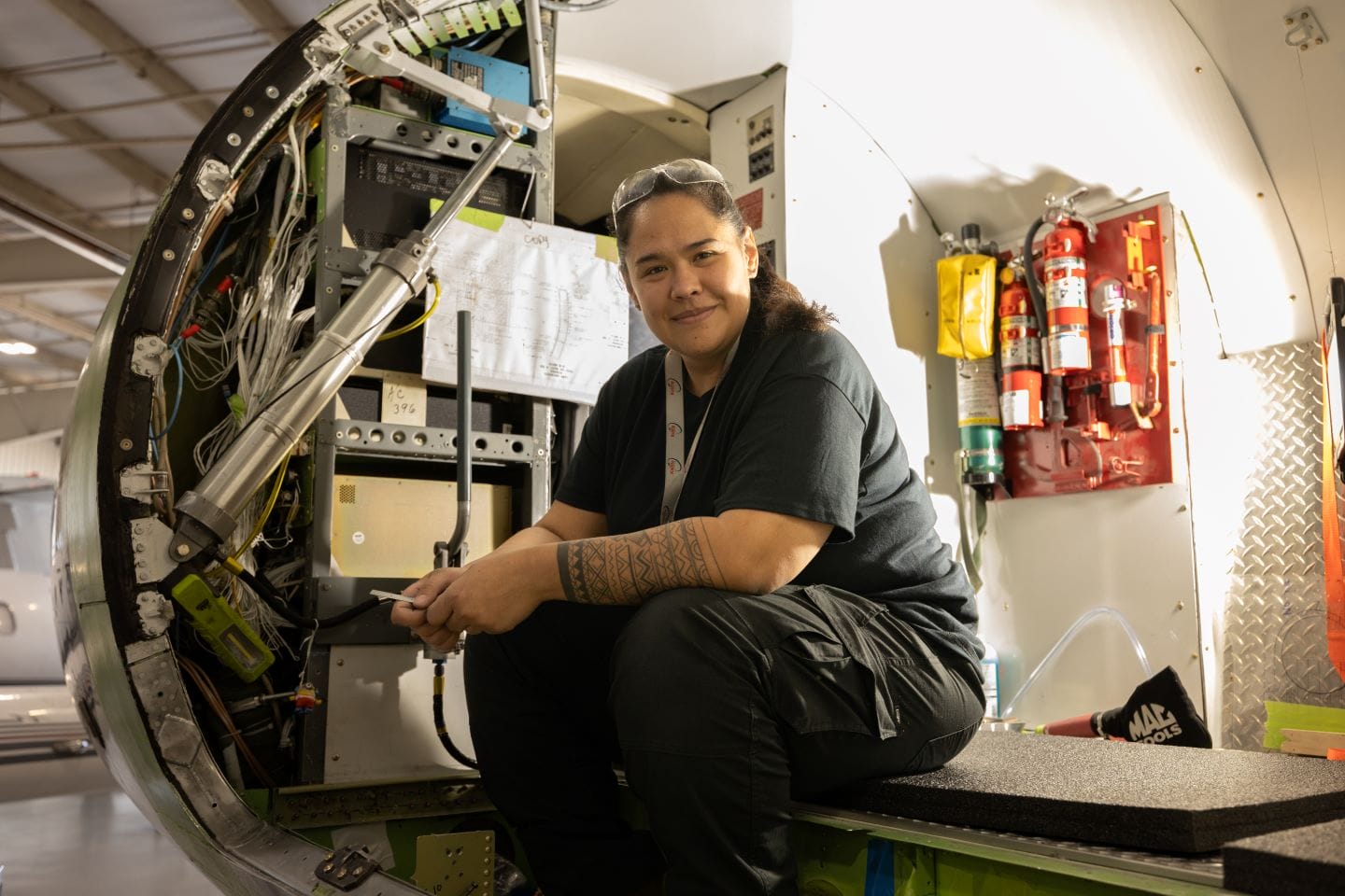 Aircraft mechanic sitting inside an open jet compartment with wiring and equipment
