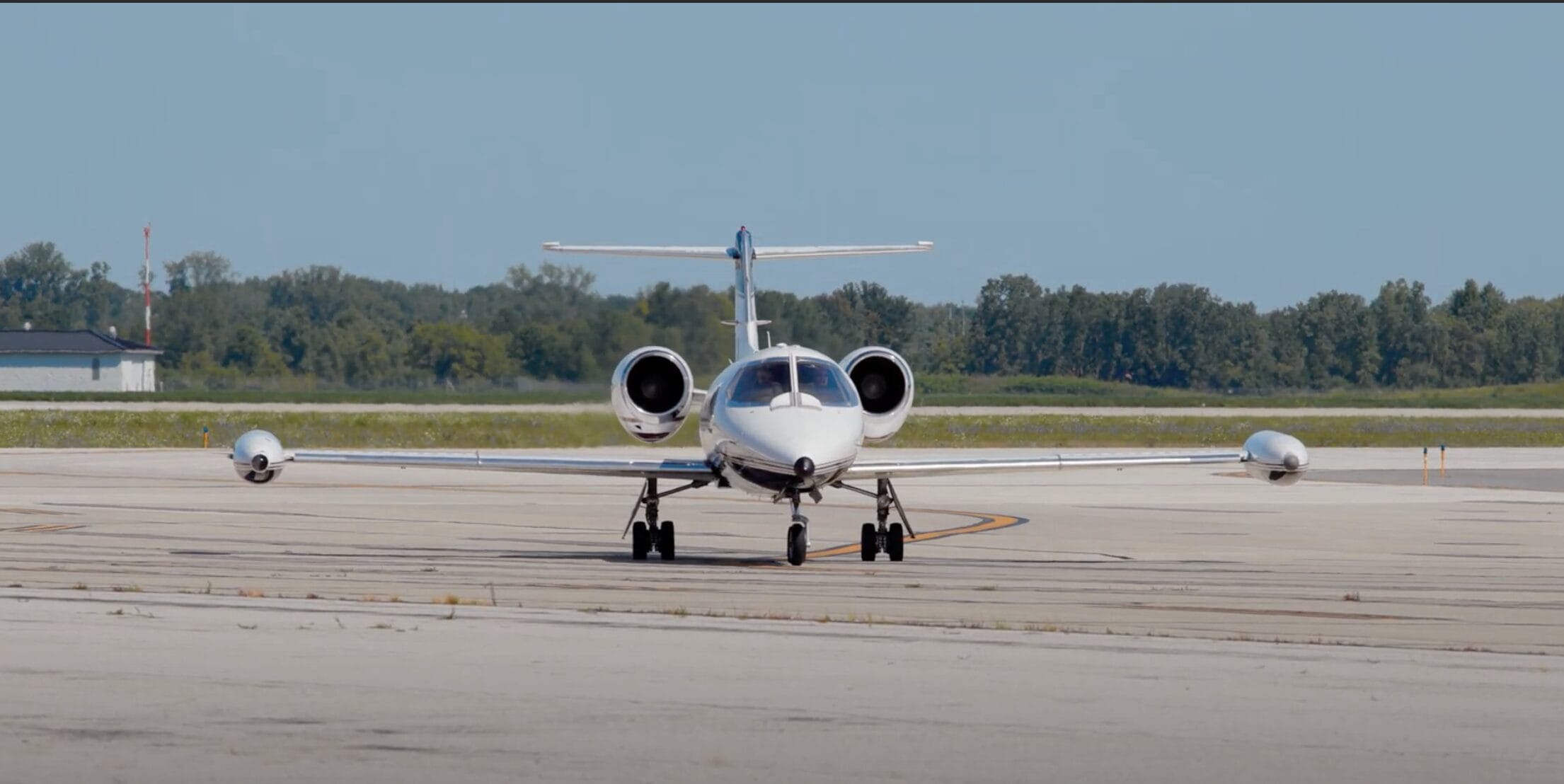 Small private jet taxiing on a runway with trees in the background