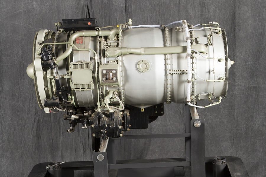 General Electric CJ610 turbojet engine on display, showing detailed components including the compressor, combustion chamber, and exhaust assembly, mounted on a black support stand.