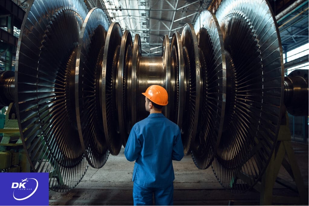 Engineer inspecting a large industrial turbine rotor in a manufacturing facility, focusing on precision blades and rotable parts for quality assurance and certification compliance. The image reflects DK Turbines’ commitment to certified turbine component services, with their logo visible in the corner.